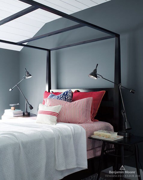 A bedroom featuring a black four-poster bed, dressed with red and white bedding and black side tables decorated with books and lamps. The walls are painted in Wolf Gray 2129-20.