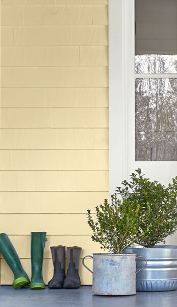 A vignette of a porch with wellington boots and planters in front of painted wooden cladding in Aura Eggshell Weston Flax HC-5 and doorway architrave in Aura Exterior Satin Chantilly Lace OC-65